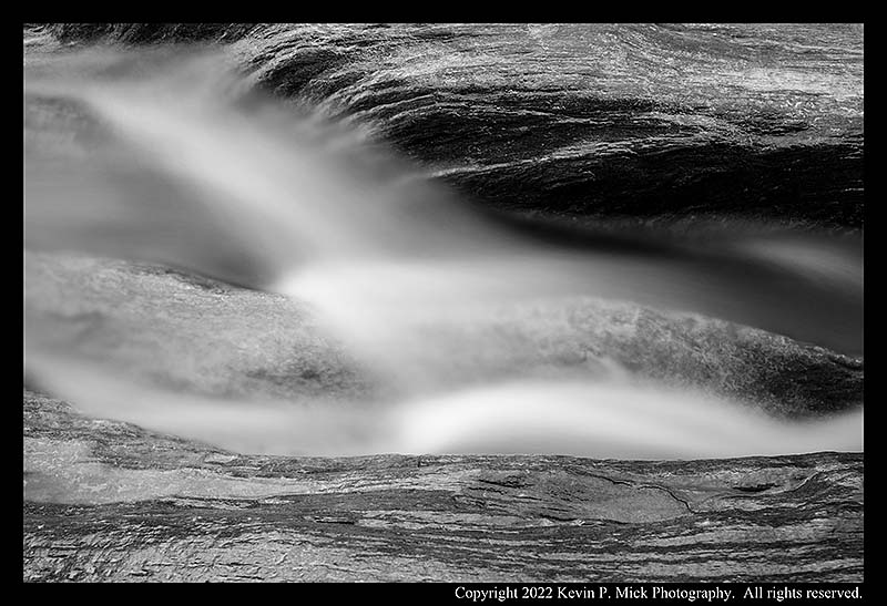 BW photograph of water running through boulders.