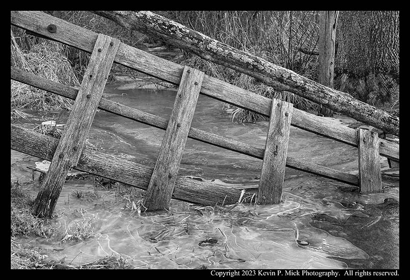 BW photograph of a broken fence frozen in ice.
