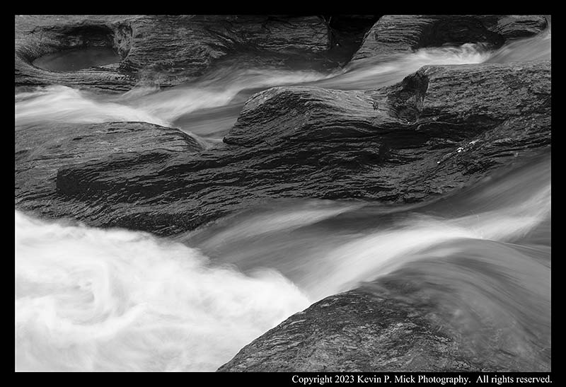 BW photograph of post-rain water flowing between rocks in a local waterway.