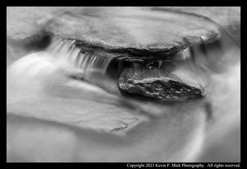 BW photograph of water running over several rock shelves.